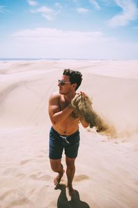 Full length of shirtless man standing on sand at beach