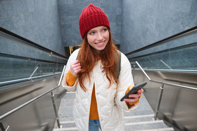Portrait of young woman standing against escalator