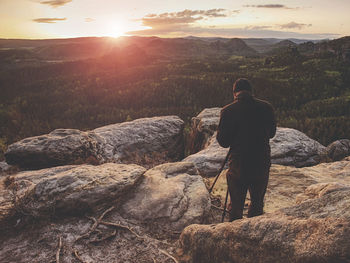 Photographer on mountain cliff take picture of landscape awaking. dreamy foggy spring orange mist