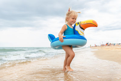 Full length of young woman exercising at beach against sky