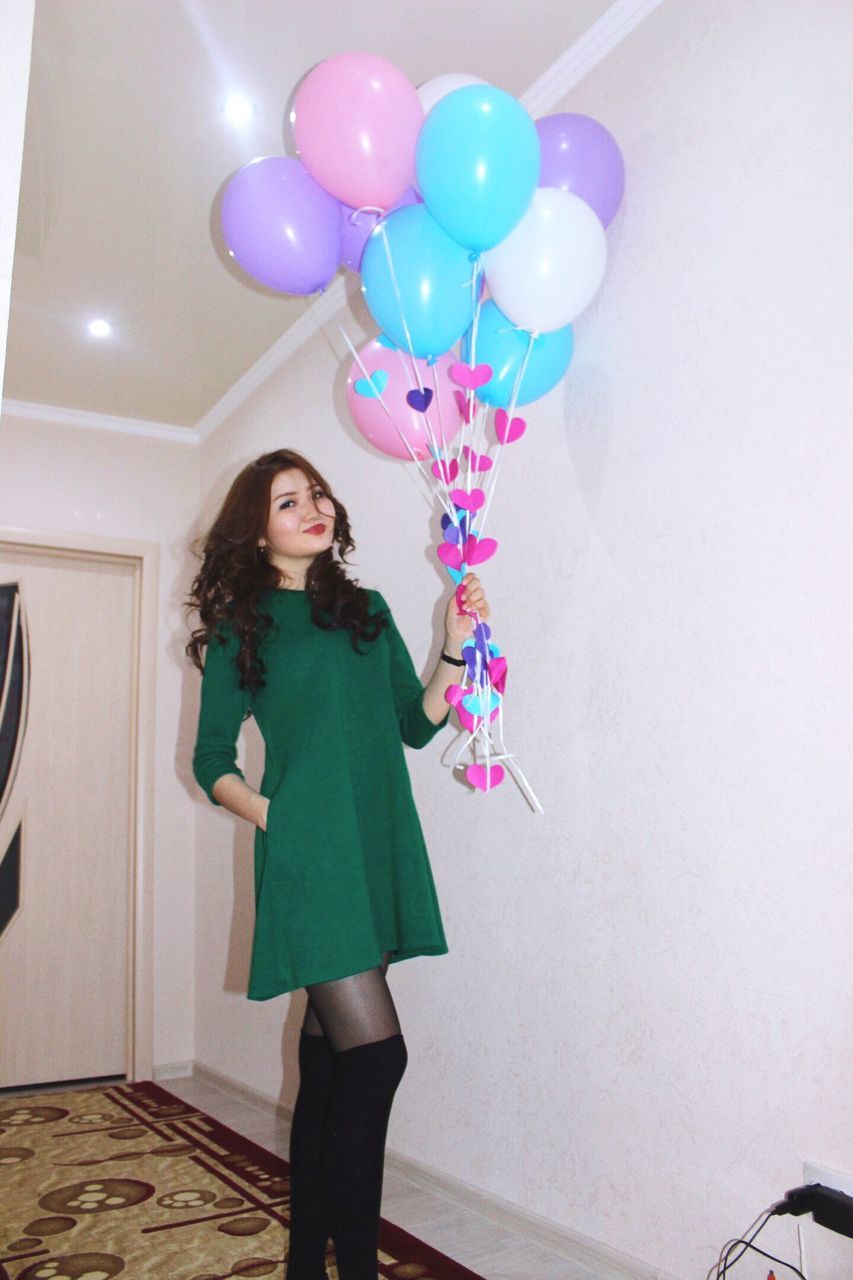 lifestyles, leisure activity, standing, casual clothing, indoors, young adult, full length, front view, young women, person, wall - building feature, balloon, blue, three quarter length, multi colored, looking at camera, fun, fashion