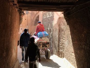 Rear view of people in alley amidst buildings during sunny day