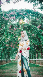 Woman standing by flowers against trees