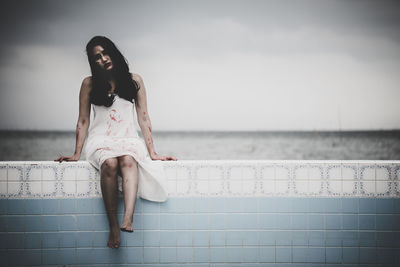 Woman sitting by sea against sky