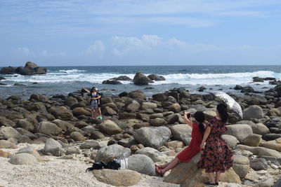 People on rocks at beach against sky