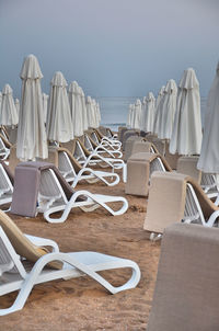 Empty chairs and tables and umbrellas at beach against sky