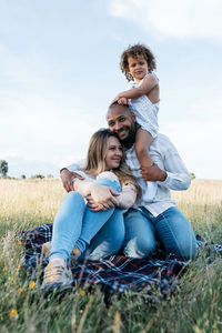 Side view of cheerful multiracial couple with adorable little daughter playing in meadow in summer