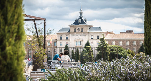 People sitting on chairs outside building against sky