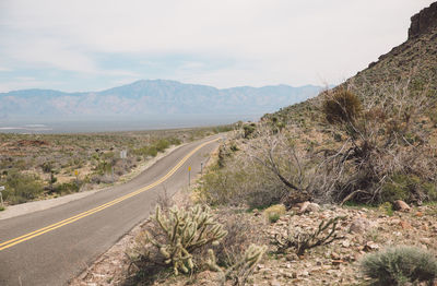 Empty country road passing through arid landscape against sky