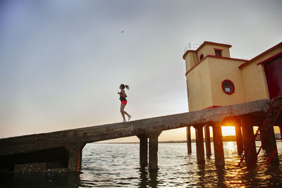 Woman jogging on pier over sea during sunset