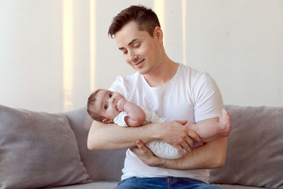 Father carrying baby while sitting on sofa at home