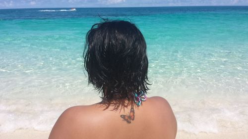 Rear view of woman with tattoo standing at beach against sea