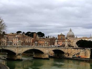 Bridge over river in city against cloudy sky