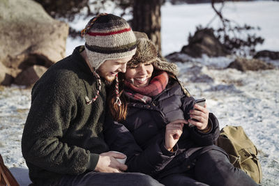 Couple using smart phone while relaxing on snow covered field