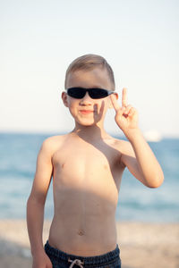 Portrait of shirtless boy standing at beach against sky