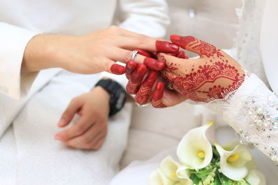 Midsection of bride putting ring in groom finger sitting on sofa during wedding