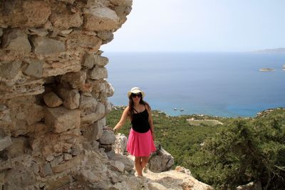 Young woman wearing sunglasses standing on cliff against sea