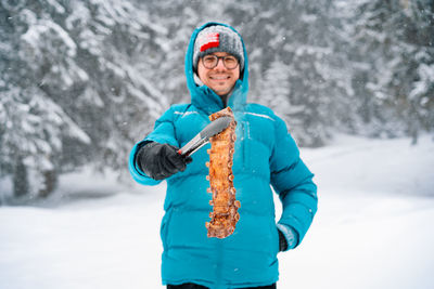 Smiling man holding pork ribs in snowy winter forest