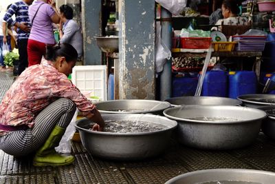 Woman crouching by container with water at market