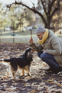 Full length of man crouching while talking with dog at park during autumn