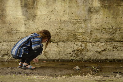 Side view of woman crouching by puddle on field