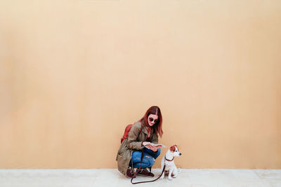Woman with dog sitting against wall