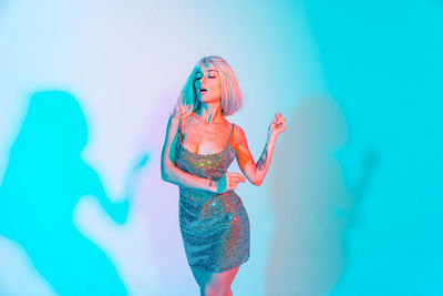 Young woman in dress dancing against illuminated background