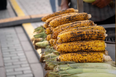 Freshly roasted corn on the cob is stacked neatly at a bustling outdoor market, enticing visitors