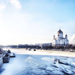 Frozen river by church against sky