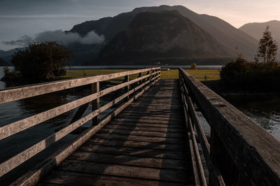 Wooden footbridge over river leading towards mountains against sky