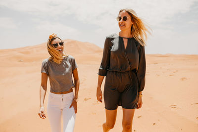 Smiling friends walking on desert in sunny day