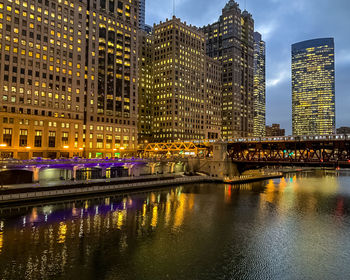 Illuminated bridge over river by buildings against sky at night