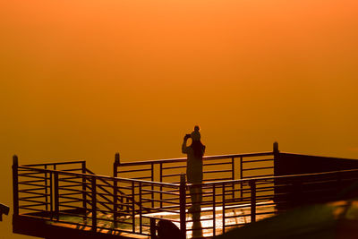 Man standing by railing against orange sky