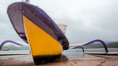 Close-up of yellow boat moored at sea shore against sky