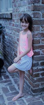 Portrait of smiling young woman standing against brick wall