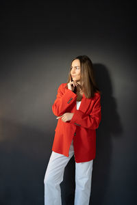 Young women in the red suit near a dark gray background in thinking pose