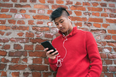 Full length of man using mobile phone against brick wall