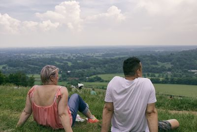Rear view of friends sitting on land against sky