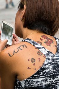Rear view of woman with floral tattoo using smart phone