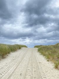 Dirt road amidst land against sky