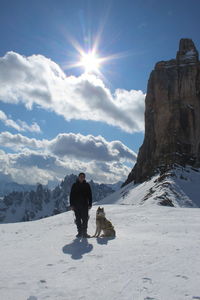 Full length of man with dog on snow capped mountain against sky during winter