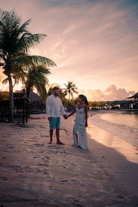 Couple holding hands standing on beach during sunset