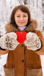 Portrait of smiling girl with heart shape in hands in winter forest. happy valentines day. 