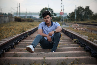 Portrait of young man sitting on railroad track