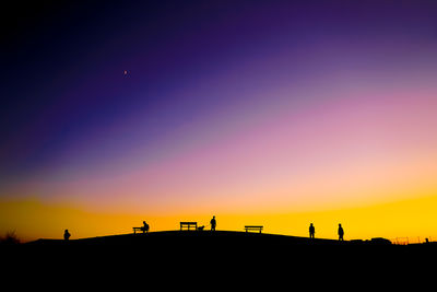 Silhouette people walking on field against clear sky during sunset