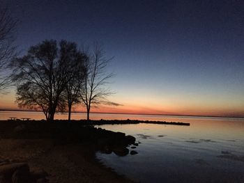 Silhouette bare tree by lake against sky during sunset