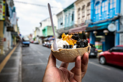 Midsection of person holding ice cream on street in city