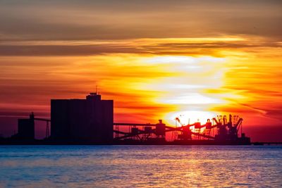 Silhouette built structure by sea against orange sky