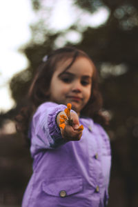 Low angle portrait of cute girl holding flowers while standing in park during sunset