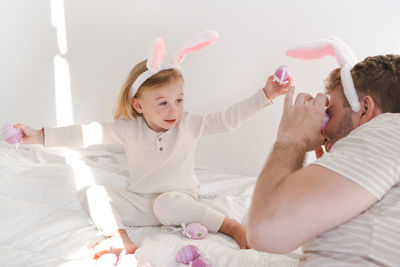 Side view of father and daughter playing with eggs wearing rabbit ears. easter concept